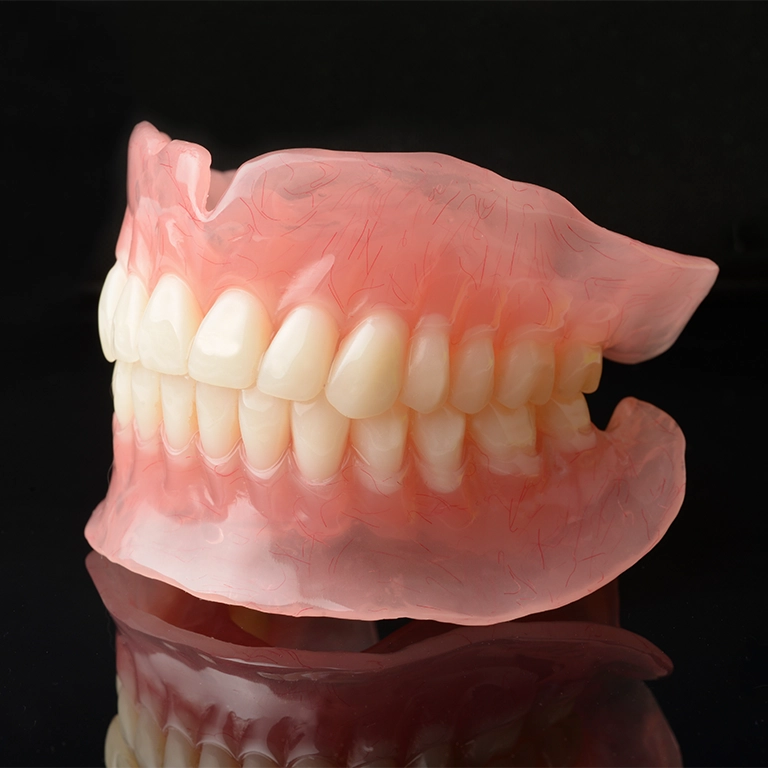 Set of full upper and lower dentures with pink gum base displayed on black surface at Smile Circle Dental