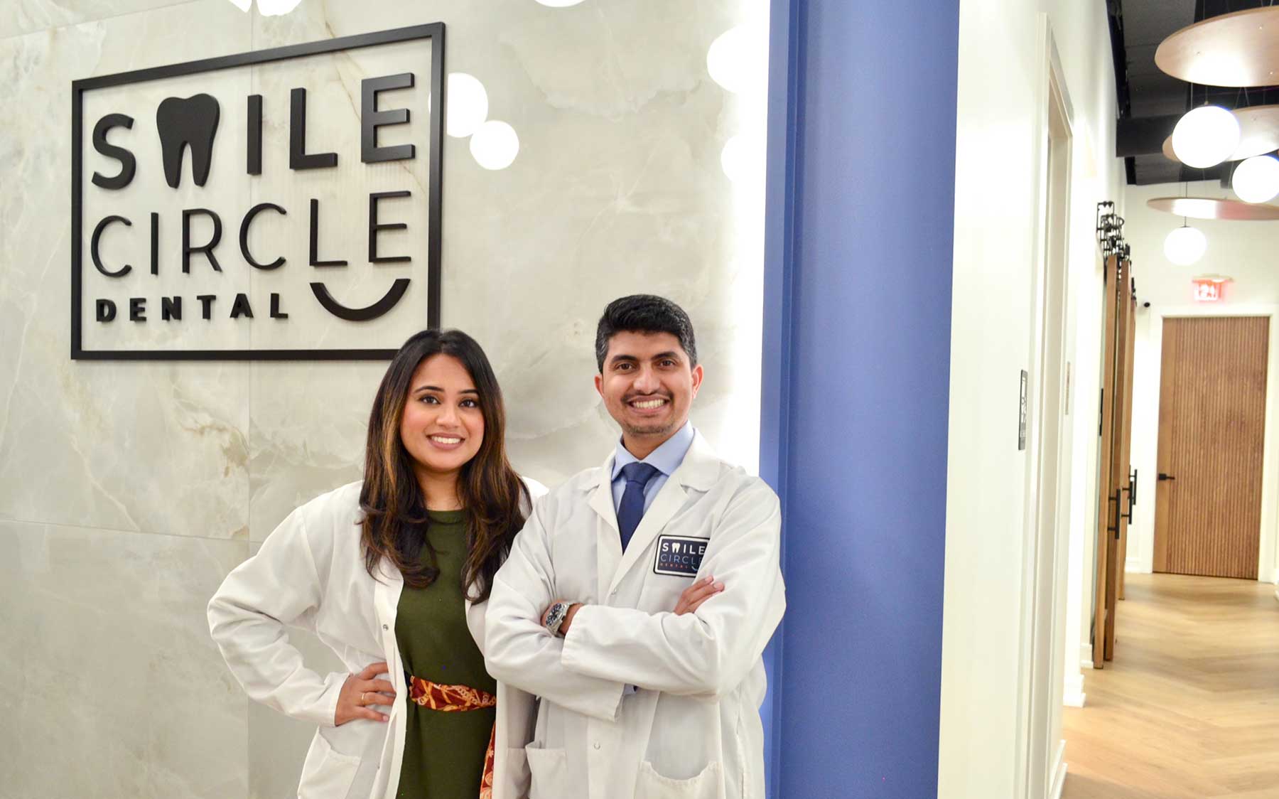 Two dentists at Smile Circle Dental smiling together in the clinic hallway beside the logo wall