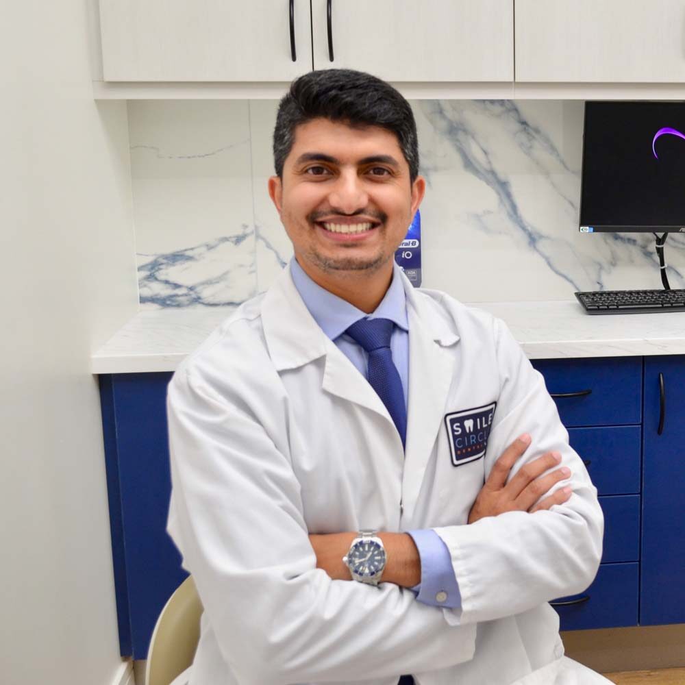 Smiling dentist in a white coat with the Smile Circle Dental logo, posing confidently in a modern clinic